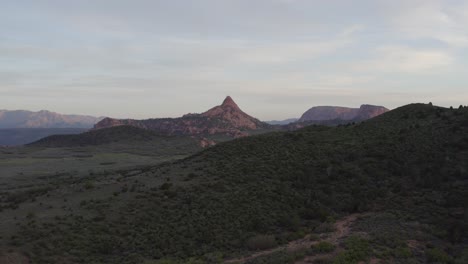 Slowly-tracking-in-over-a-hill-to-reveal-a-sunset-view-of-Zion-National-Park-with-large-cliffs-and-rock-formations