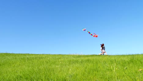 children run down the green hill with a flying kite