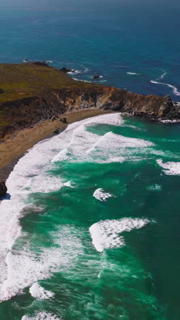 sunny scenery of morro bay rocky coastline at daytime. low white waves coming to the narrow line of a sandy beach. top view. vertical video