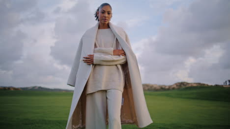 modelo elegante posando campo en el cielo nublado. mujer de cabello negro sereno admirando verde