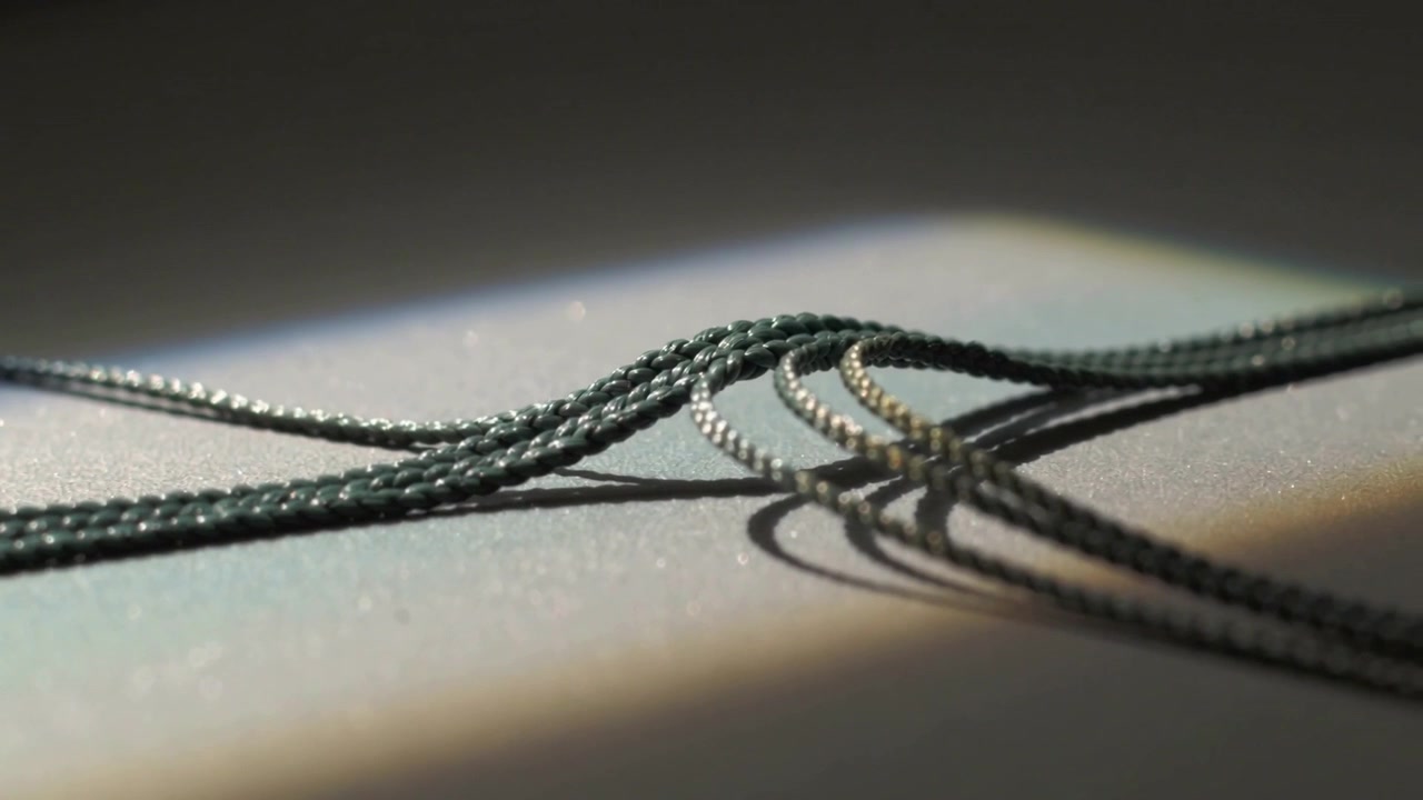 Shifting braided cords on glitter mat as light shifting, catching rectangular beam casting shadows