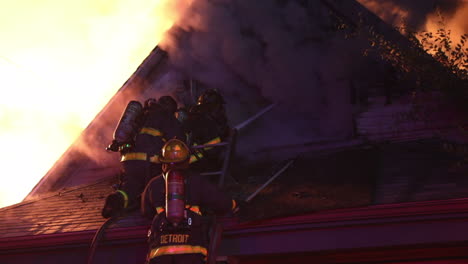 firefighters on the roof of a house get up close to a blazing fire and attempt to combat the blaze with a fire hose