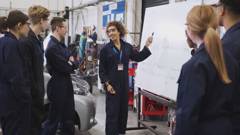 female tutor by whiteboard with students teaching auto mechanic apprenticeship at college