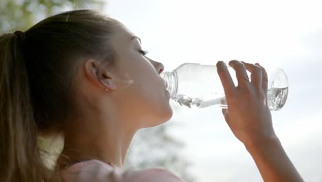 woman standing in front of lake drinking water from bottle