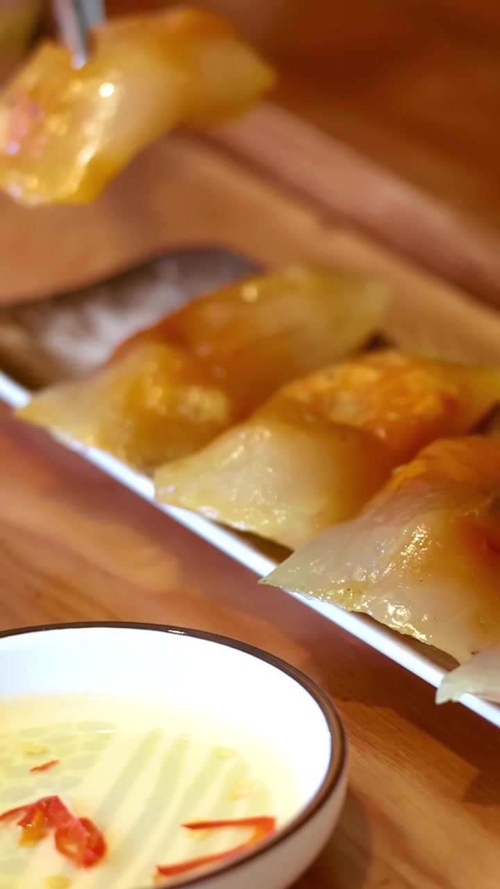 Chopsticks lift a translucent Vietnamese shrimp dumpling from a plate on a wooden table