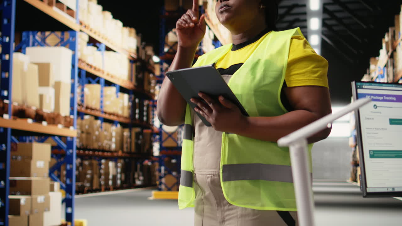 Vertical Video African american female staff in hi vis vest counts packages on industrial racks