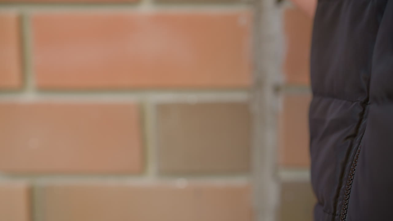 close up of person hand holding vaping device with fingers gently gripping it while standing near brick wall in soft daylight as person begins to lift device for inhalation