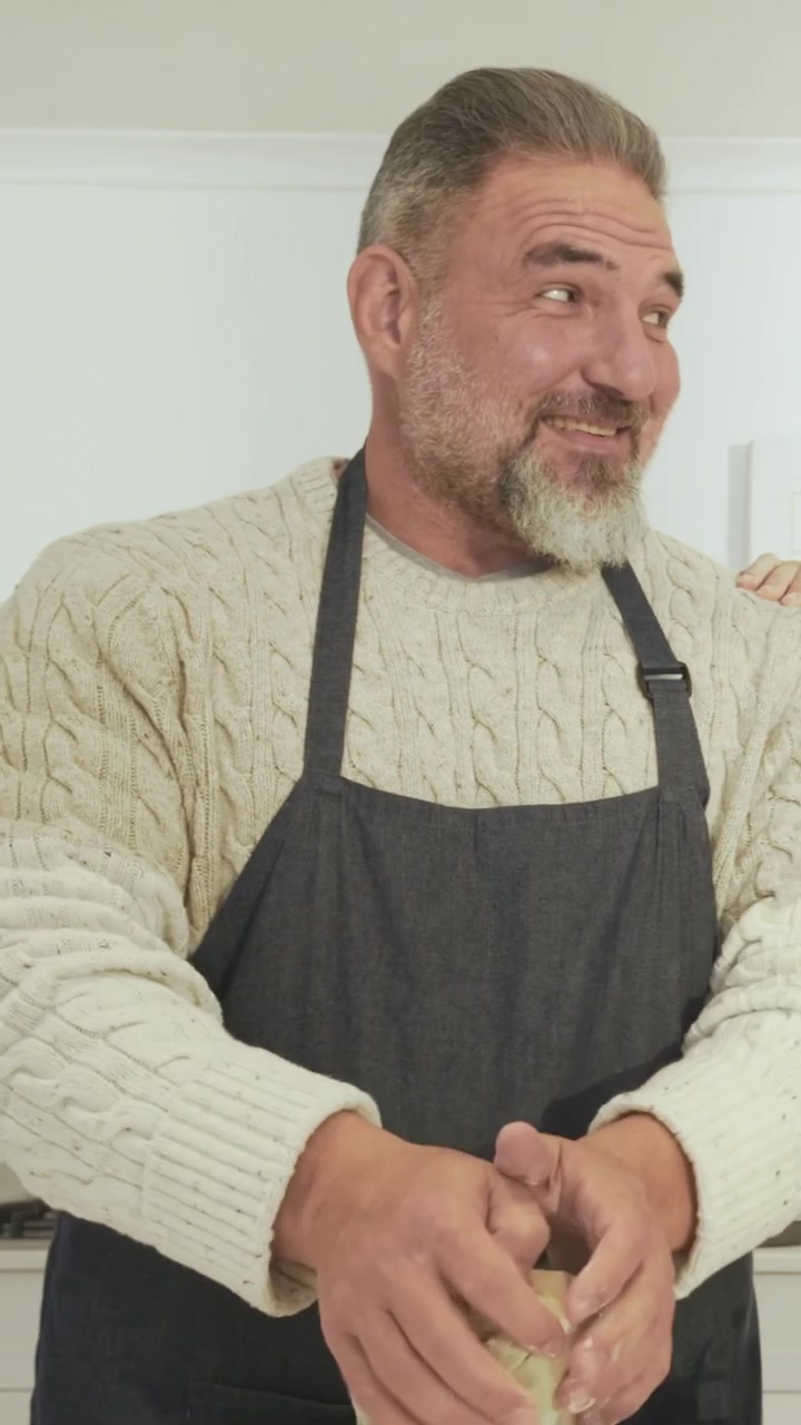 Video vertical: Hombre amasando masa después de que su pareja le dé un toque en el brazo en la isla de la cocina, con crema de chocolate