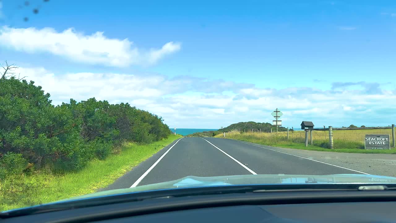 A car journey along the Great Ocean Road, capturing coastal landscapes under bright daylight with a clear blue sky