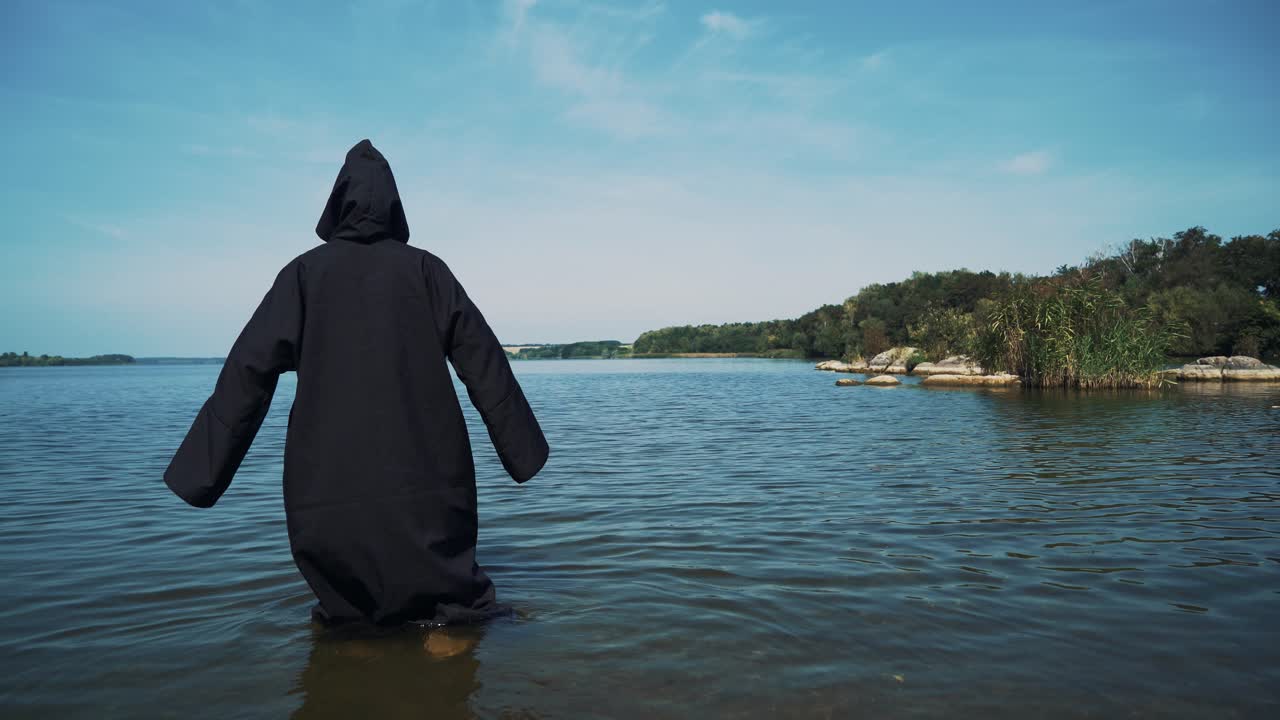 Terrible witch in black mantle in the water outdoor.