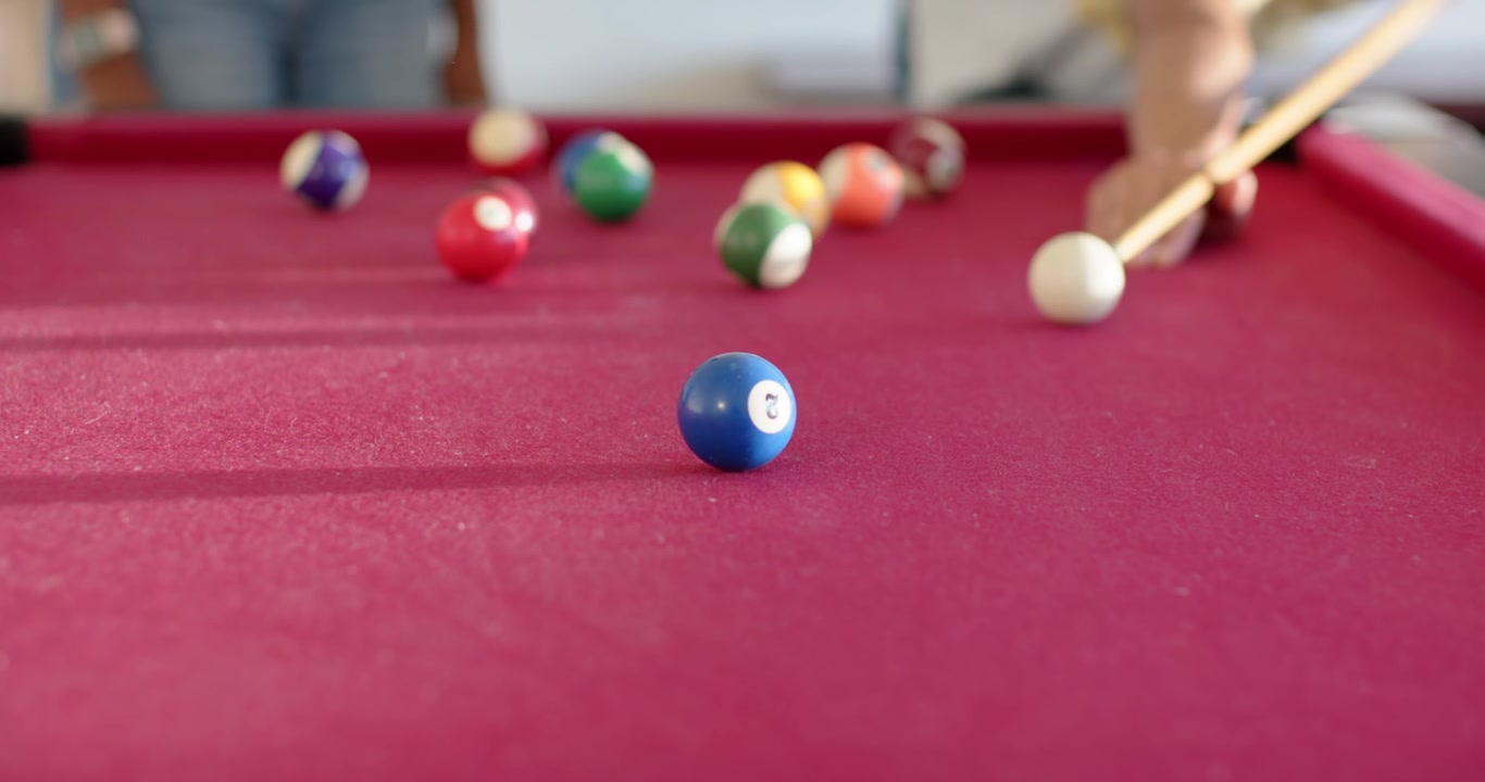 African American friends playing pool, woman hitting cue ball, sending blue 2 rolling at home table