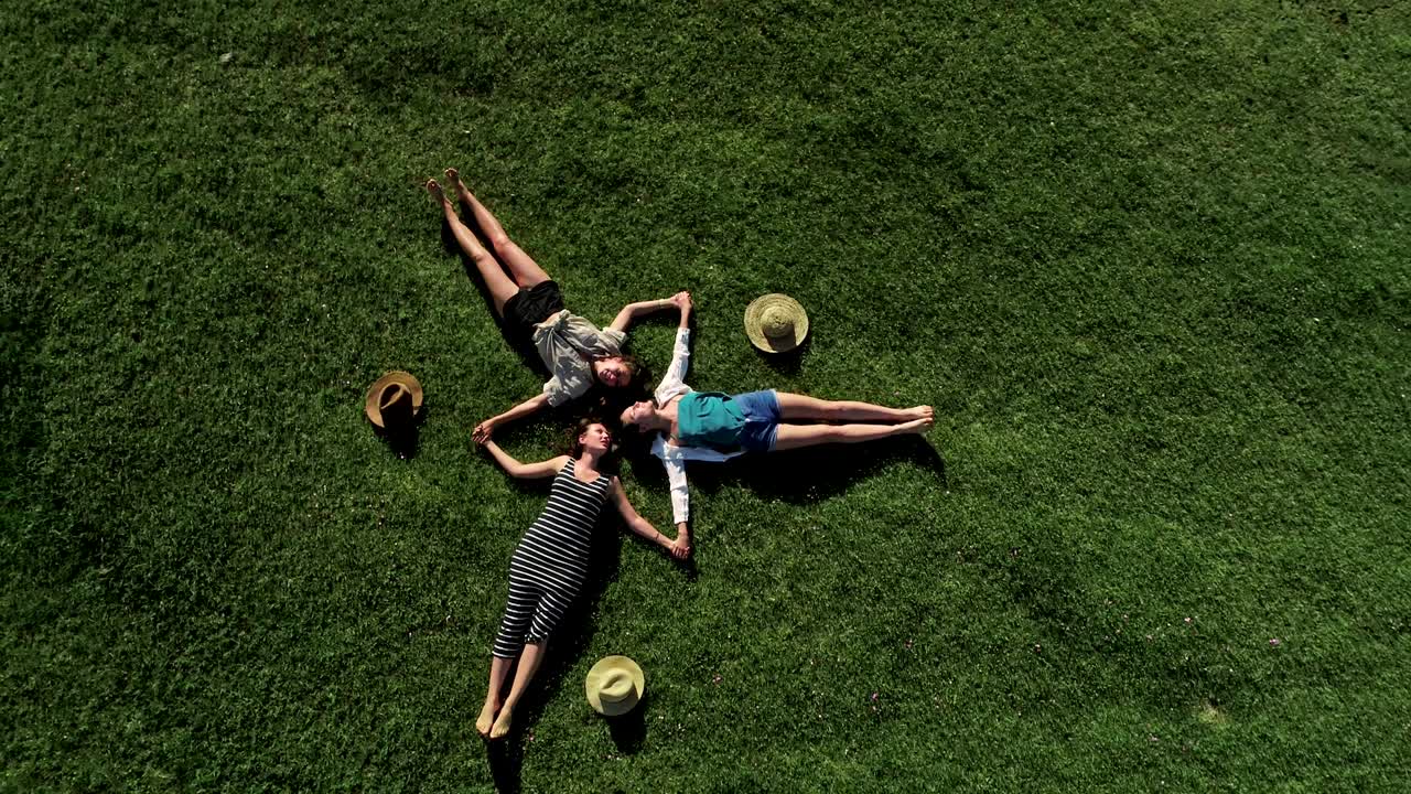 초록 잔디 위에 누워있는 세 명의 매력적인 소녀들이 잔디에서 즐거움을 즐기고 있습니다.