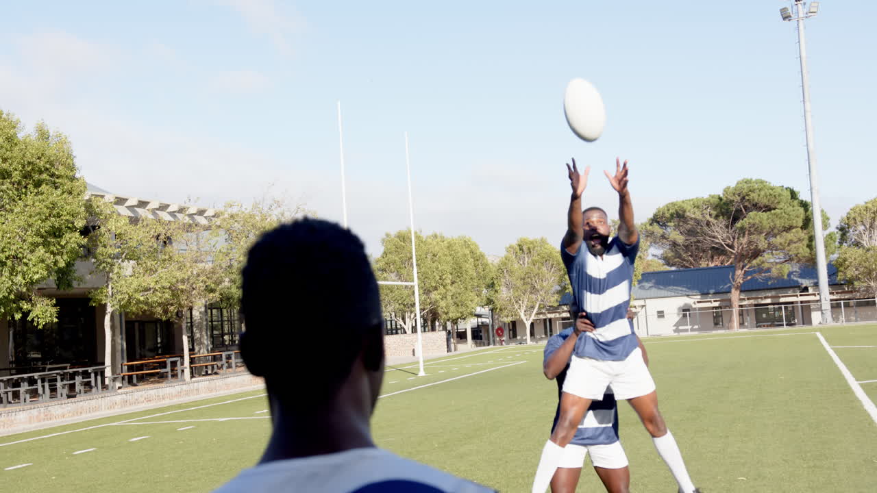 Playing rugby, african american men jumping to catch ball on field during practice session