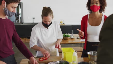 cocinera caucásica que enseña a un grupo diverso usando máscaras faciales