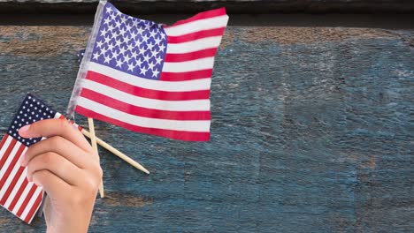 Animation-of-person-holding-american-flag-on-wooden-background