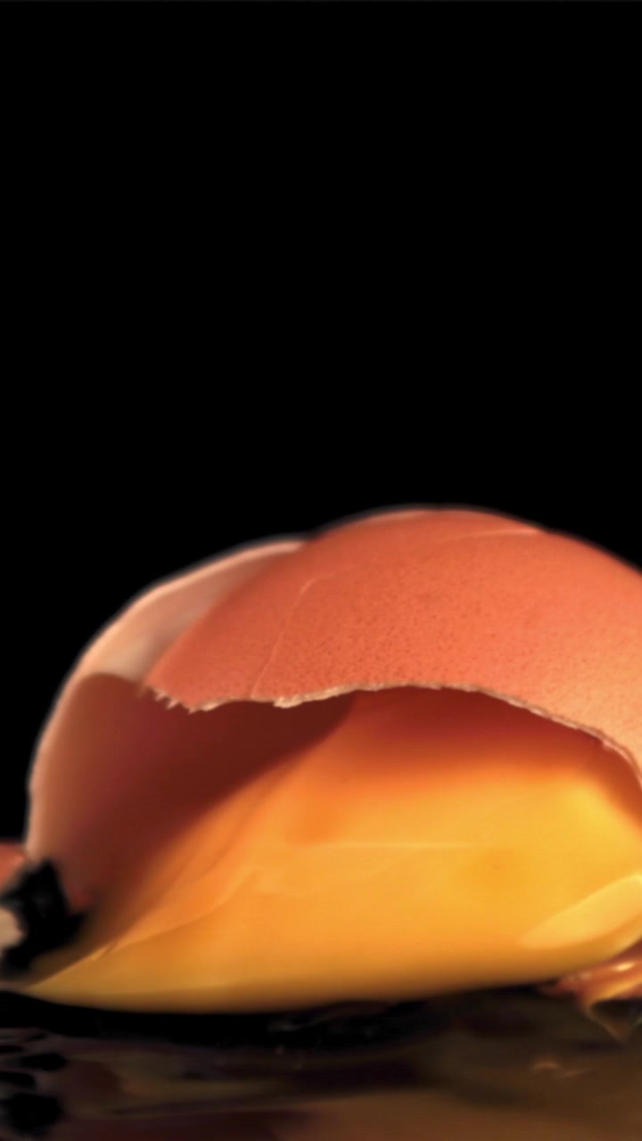 Slow Motion Egg Cracking and Yolk Spilling on Black Background