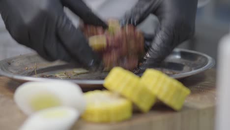 las manos de los cocineros con guantes de blsck frotan un pedazo de ternera en la placa de metal, marinando la carne.