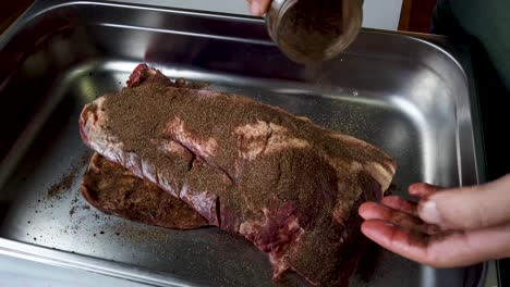 el hombre vierte una mezcla de condimentos secos sobre la carne cruda, la frota para prepararla para fumar