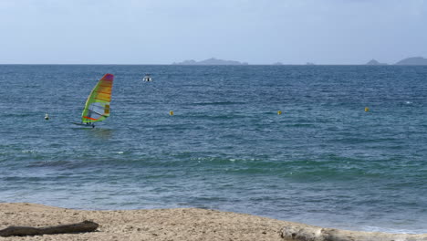 Windsurfer-Gliding-Across-Turquoise-Ocean-Surface-by-the-Beach