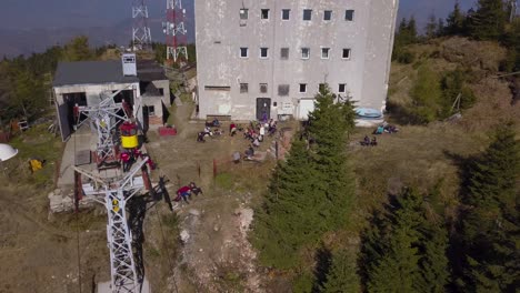 heniu summit, romania - hikers taking a break near a building and towers surrounded by green pine trees in the mountain on a sunny day - aerial drone shot