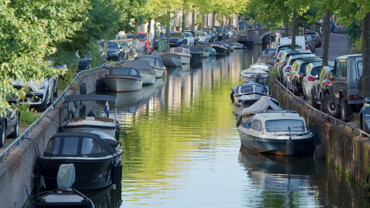 Small motorboat cruises along a tree-lined canal in Haarlem, Netherlands on a sunny summer day