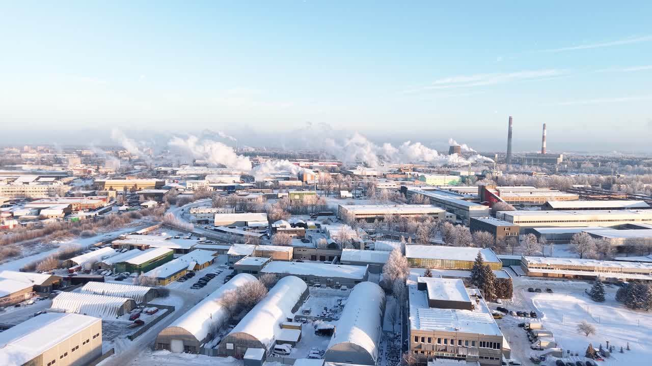Drone video capturing a vast industrial cityscape under a blanket of snow. Towers emit steam as the sun casts a cold, clear light. The sweeping aerial view highlights expansive urban infrastructure