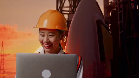 primer plano de una ingeniera asiática con casco de seguridad trabajando en una computadora portátil mientras está de pie con el transbordador espacial, hora de la puesta del sol