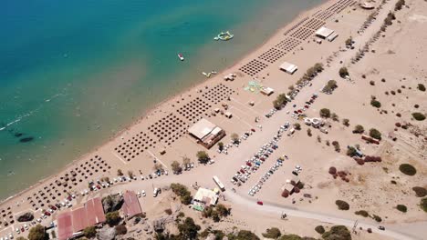 Costa-De-Arena-Dorada-Con-Sombrillas-Nipa-Y-Vehículos-Estacionados-Durante-El-Verano-En-La-Playa-De-Tsambika,-Isla-De-Rodas,-Grecia