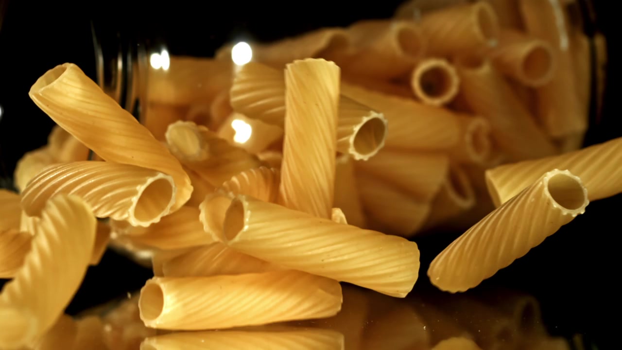 Rigatoni secchi che cadono al rallentatore su una superficie riflettente