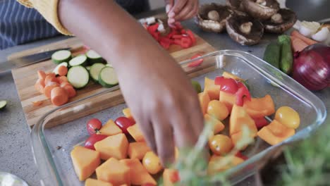 Midsection-of-african-american-woman-in-apron-preparing-vegetables-in-kitchen,-slow-motion