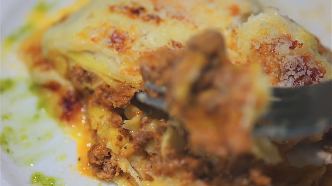 Close up of a fork picking up lasagna from a white plate