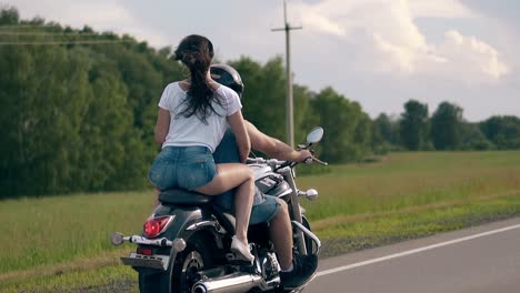 una giovane donna guida una moto moderna nera con un tizio oltre gli alberi