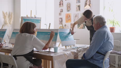 side view of a happy senior people smiling while drawing as a recreational activity or therapy in paint class together with the group of retired women and men