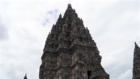 indonesia,prambanan temple on a cloudy day,camera tilts down from the top of the temple towards to the ground level, people climbing the stairs and walking around the temple complex in slow motion