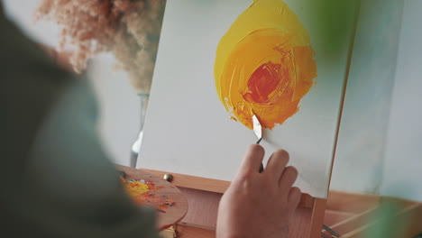 the hands of an unrecognizable man painting with a spatula on a canvas