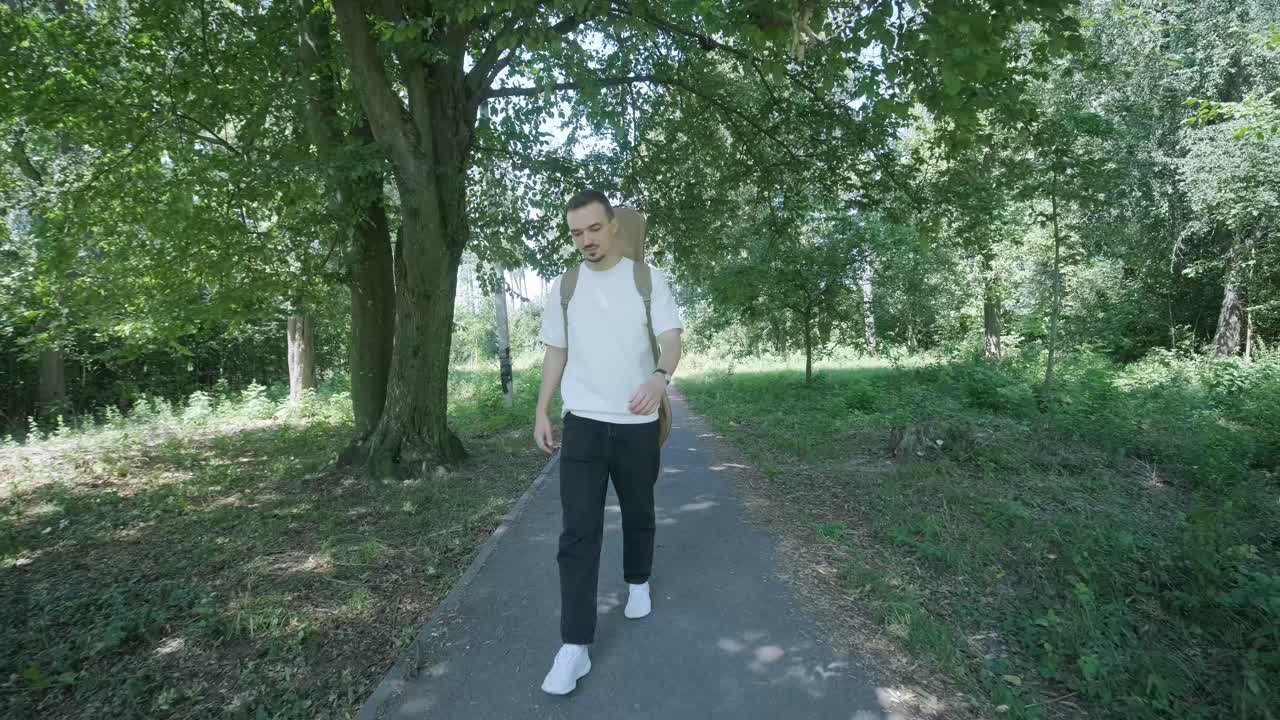 Orman yakınındaki sokakta gitarıyla yürüyen genç adam.