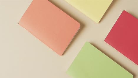 overhead view of colourful notebooks arranged on beige background, in slow motion