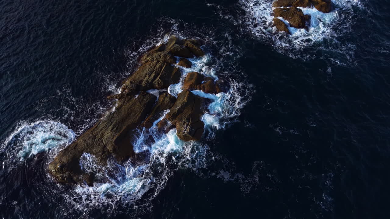 A beautiful rocky coastline with waves crashing against rugged cliffs during midday sun in a stunning coastal landscape
