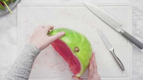 cortar la sandía roja en pedazos pequeños en una tabla de cortar blanca.