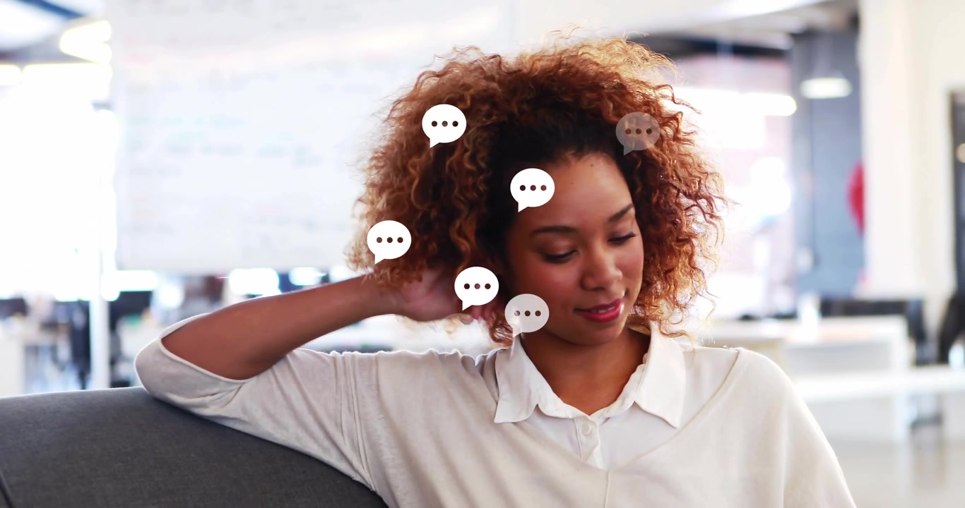 Donna che legge messaggi con bolle di chat animate che compaiono accanto alla sua testa su un divano grigio in una sala relax dell'ufficio.