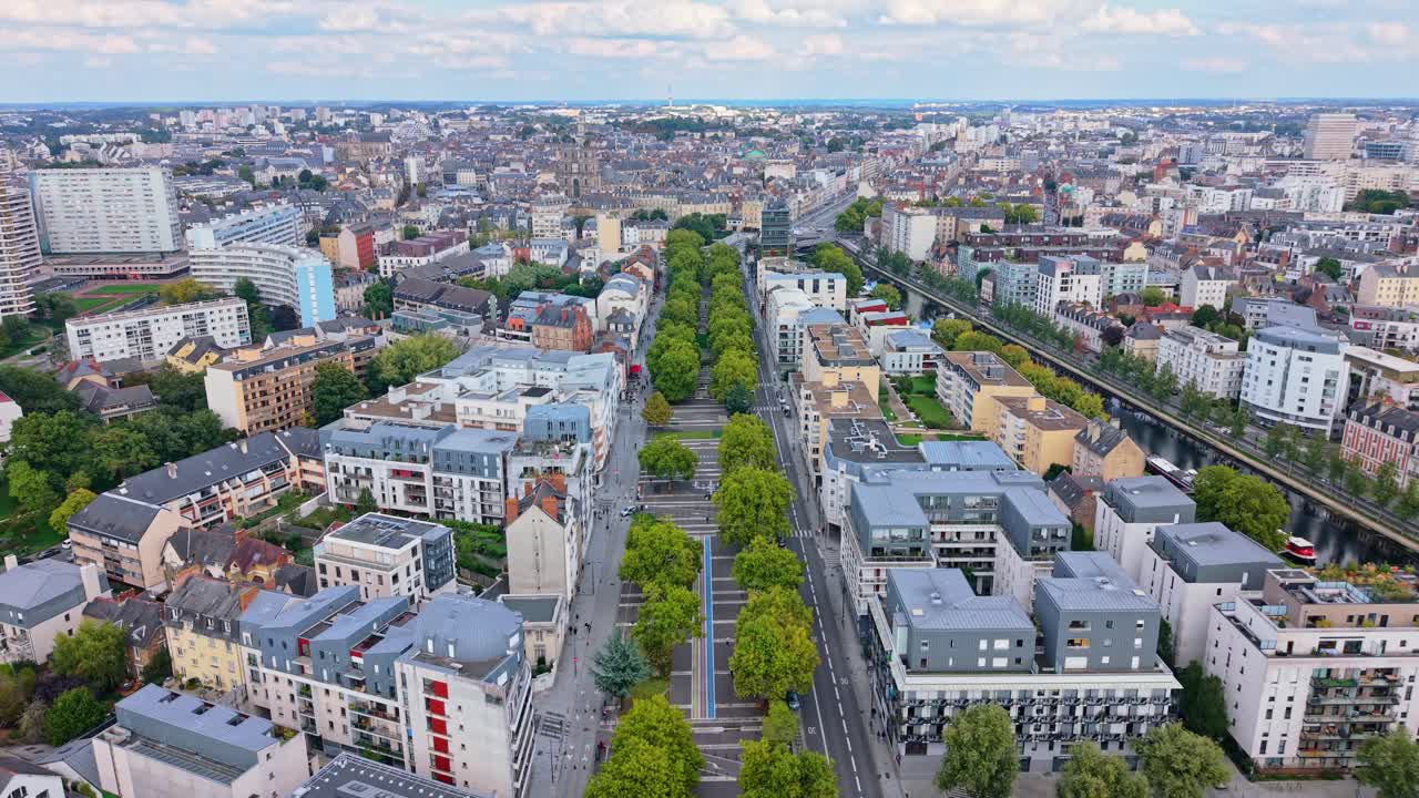 Aerial drone view flying over the Mail François Mitterrand in Rennes, France. A wide tree-lined avenue with pedestrian paths, modern buildings, and the Vilaine river nearby