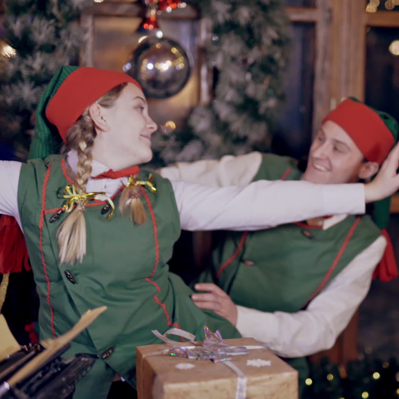 Cheerful elves in festive costumes imitate flying indoors. Happy man and woman in elf costumes are having a good time together in the room with decorations before Christmas.