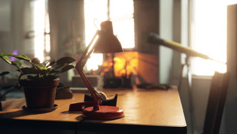 a red desk lamp on a wooden desk with a plant and a window in the background