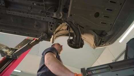 joven mecánico profesional que trabaja bajo el coche moderno levantado en el servicio de reparación de automóviles. servicio de automóviles, mantenimiento de reparación.