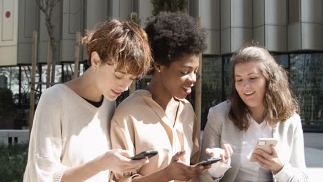 three women with smartphones sitting on street