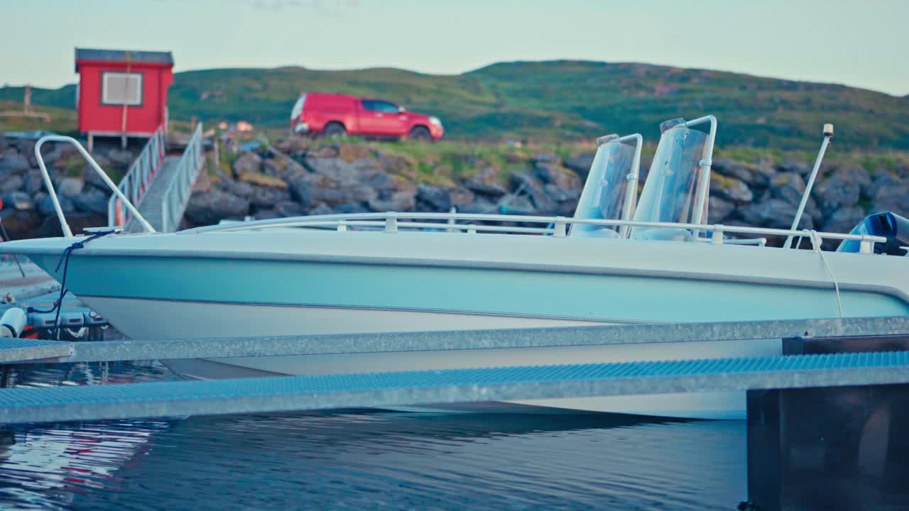 A Light Blue Boat Rests Quietly by the Dock, With a Red Cabin and Truck Standing Out Against the Green Hills of Kokelv, Norway - Close Up