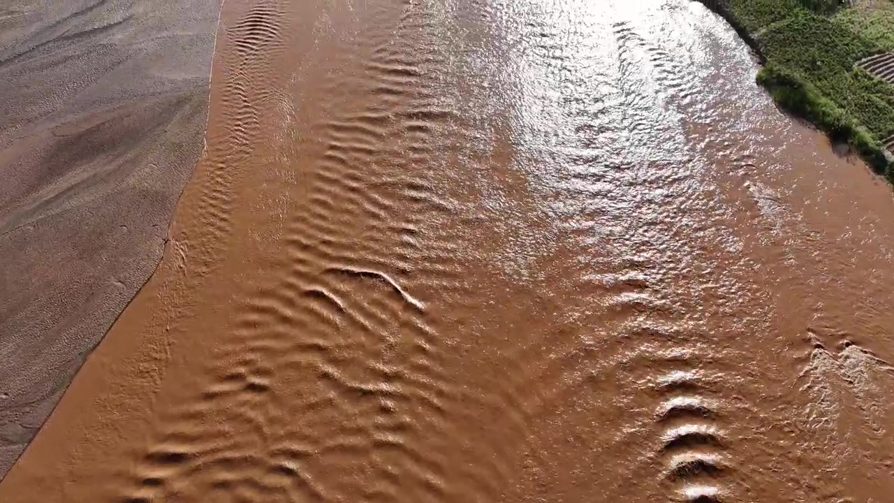 Primo piano aereo del fiume Turkwel vicino a Lodwar, Contea di Turkana, Kenya, con acqua fangosa che scorre, banchi di sabbia e la superficie increspata del fiume.