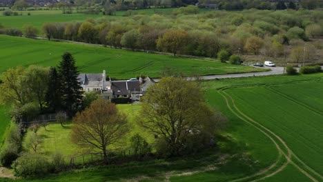 rural british farmhouse aerial orbiting view surrounded by lush green trees and agricultural farmland countryside fields