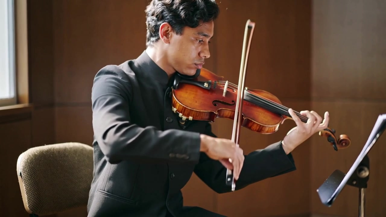 Violinista de jaqueta erguendo o arco, praticando em cadeira ao lado da janela com violino e partitura
