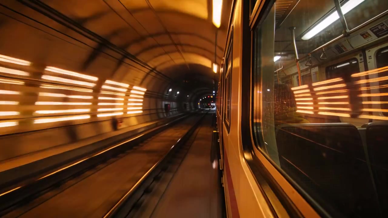 Treno che entra in un tunnel illuminato d'arancio, causando una sfocatura del riflesso del finestrino con un passeggero verso la banchina, spazio per il testo.